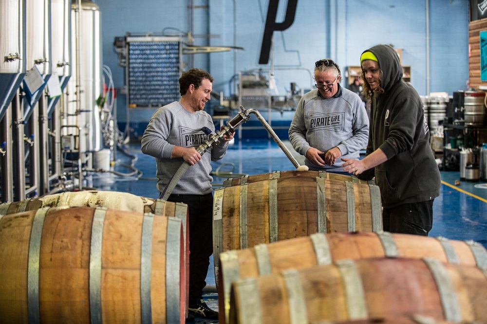 Ben Shipman from Tomfoolery Wines (left) filling up barrels with beer with Michael Cameron and Jack Cameron from Pirate Life Brewing watching